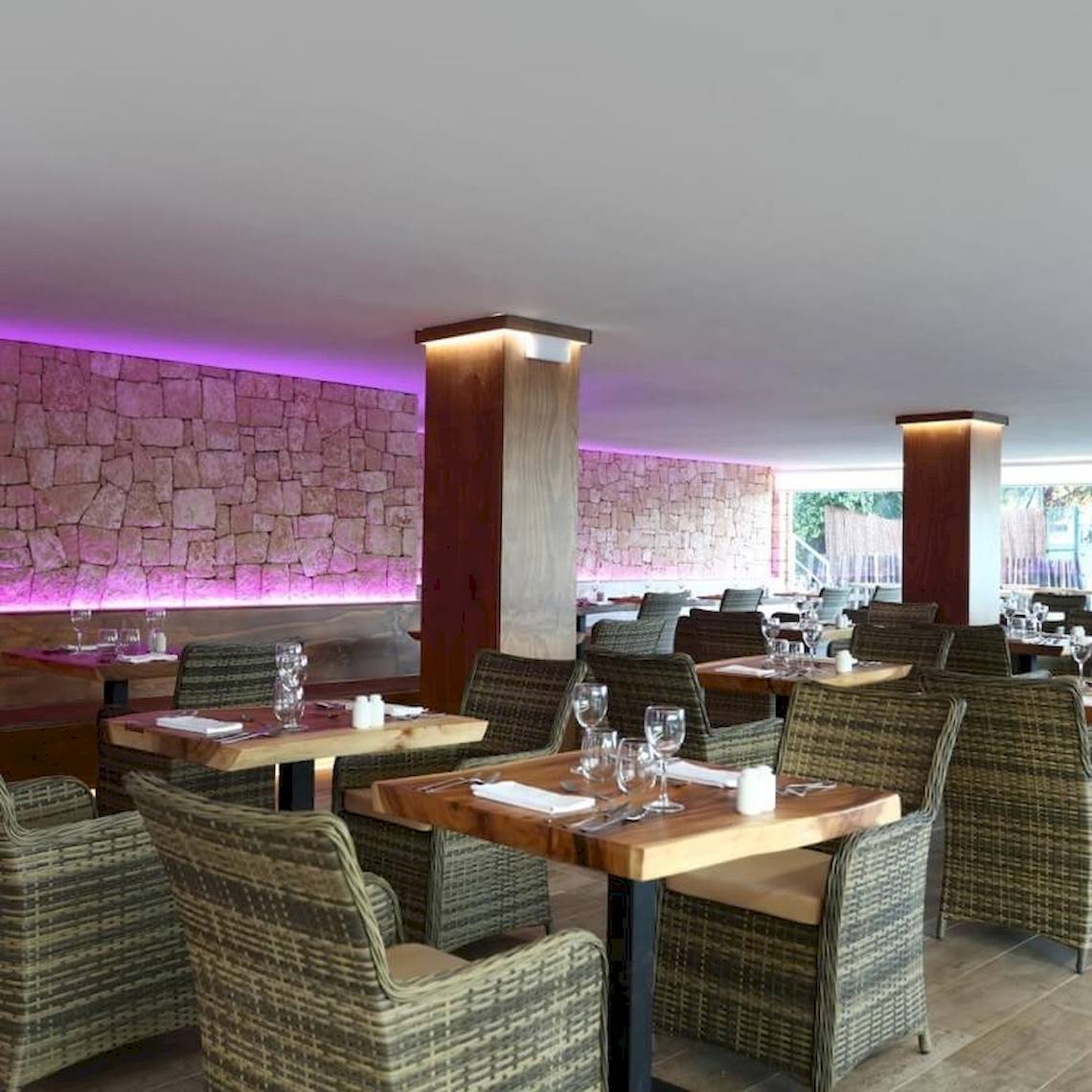 Innenansicht des Restaurants im Sandos El Greco Beach Hotel mit steinerner Wand und lila Beleuchtung.