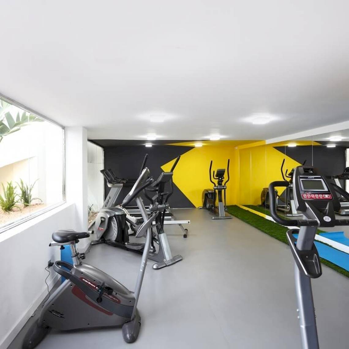 Fitnesscenter-Innenbereich im Sandos El Greco Beach Hotel mit Cardiogeräten und einer Fensteransicht.