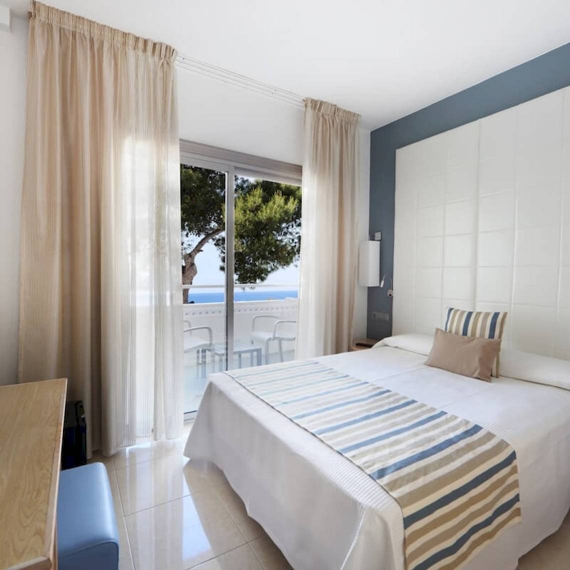 Schlafzimmer im Sandos El Greco Beach Hotel mit Blick auf das Meer und einen Balkon.