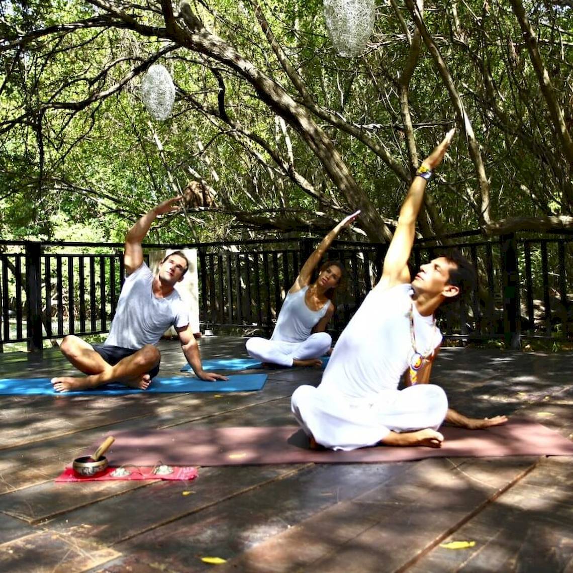 Drei Personen praktizieren Yoga auf einer Terrasse im Freien im Sandos Caracol Eco Resort.
