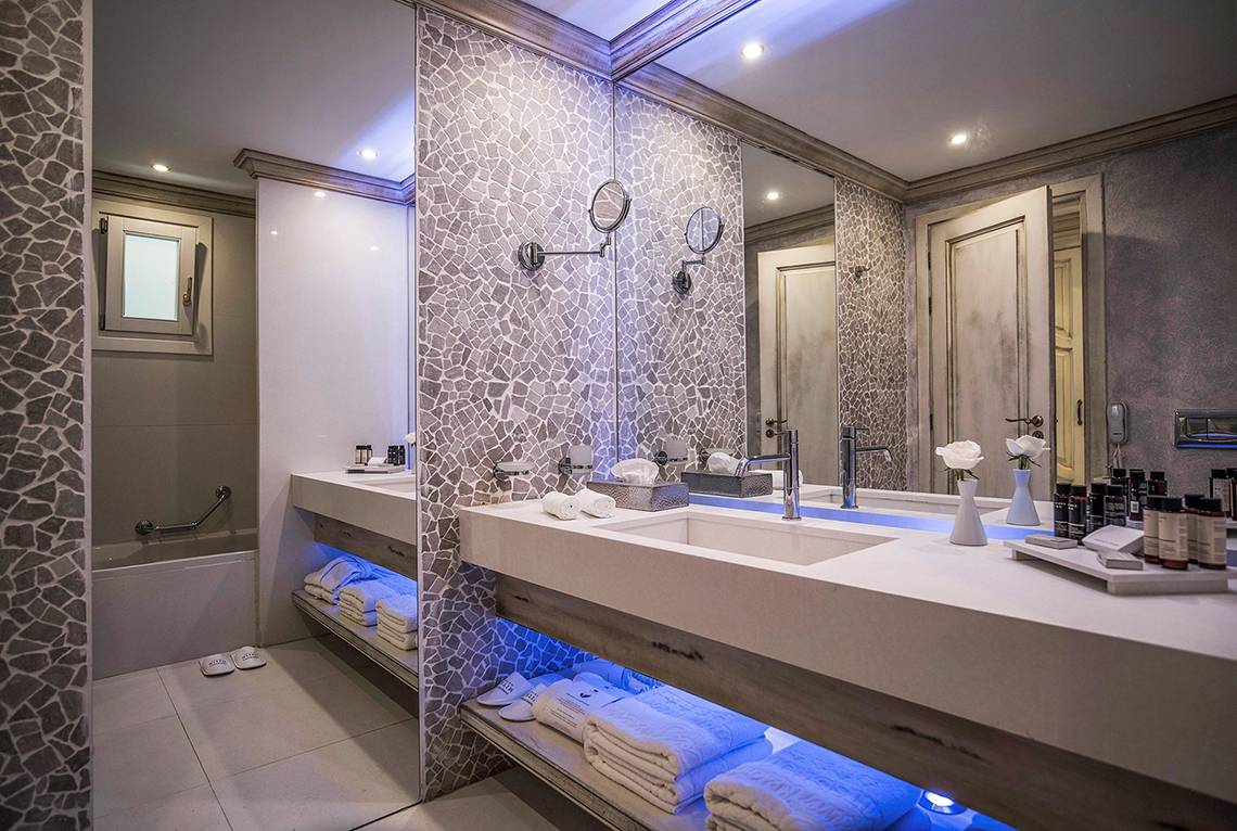 Badezimmer im Mitsis Laguna Resort mit Marmorwänden und blauen Lichtern.