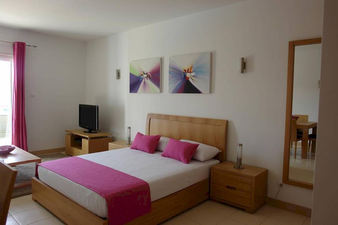 Schlafzimmer im Agua Hotels Sal Vila Verde mit einem großen Bett, Fernseher, Nachttischen und Gemälden an der Wand.