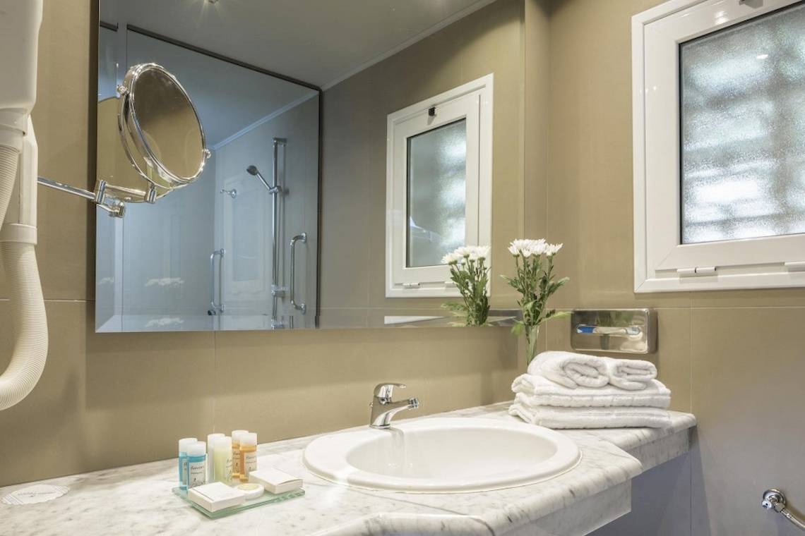 Badezimmer im Aeolos Beach Resort auf Korfu mit Spiegel, Waschbecken und Toilettenartikeln.