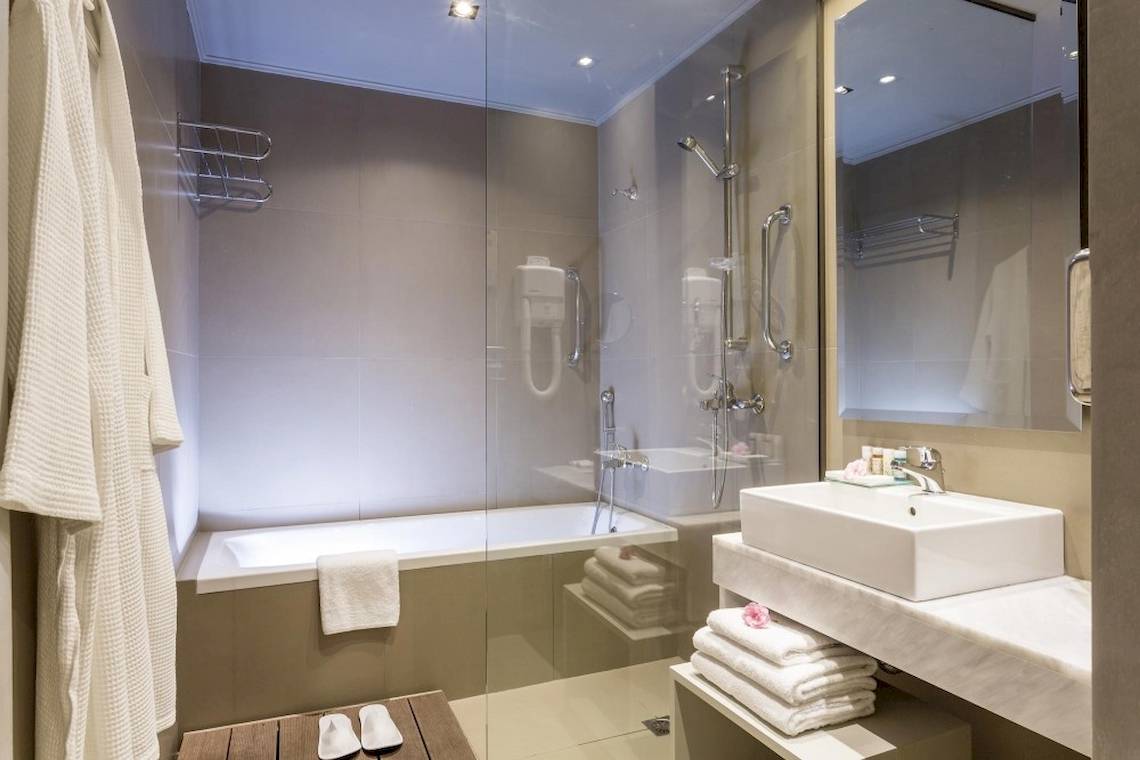 Badezimmer im Aeolos Beach Resort auf Korfu mit Badewanne, Dusche, Waschbecken und Handtüchern.