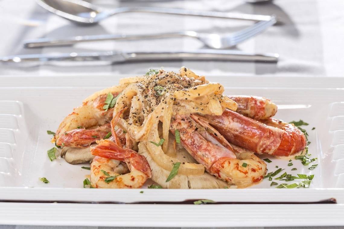 Gerecht aus Shrimps, Nudeln und Pilzen auf einem weißen Teller, serviert im Aeolos Beach Resort auf Korfu.