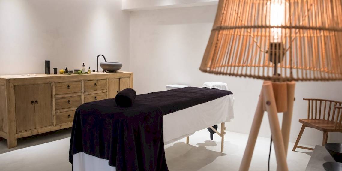Spa-Behandlungsraum im Aeolos Beach Resort Hotel mit Behandlungstisch, Lampe und Holzmöbeln.