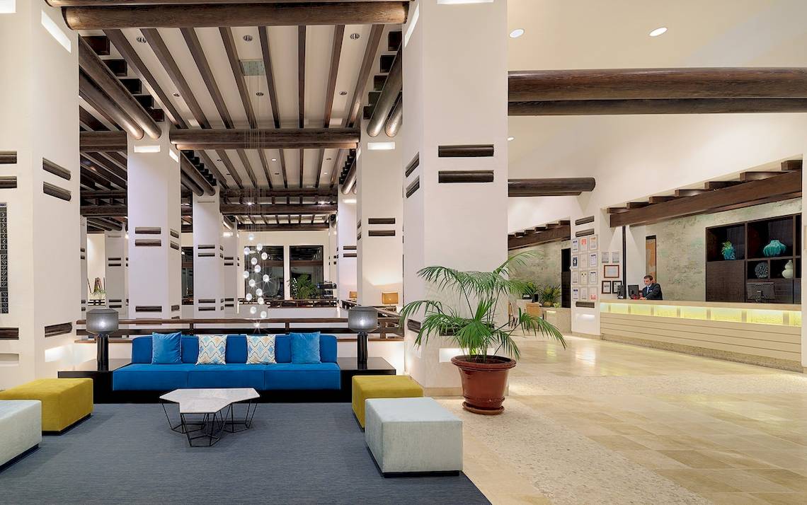 Lobby des H10 Estepona Palace mit blauer Couch, gelben Hockern und Empfangstresen
