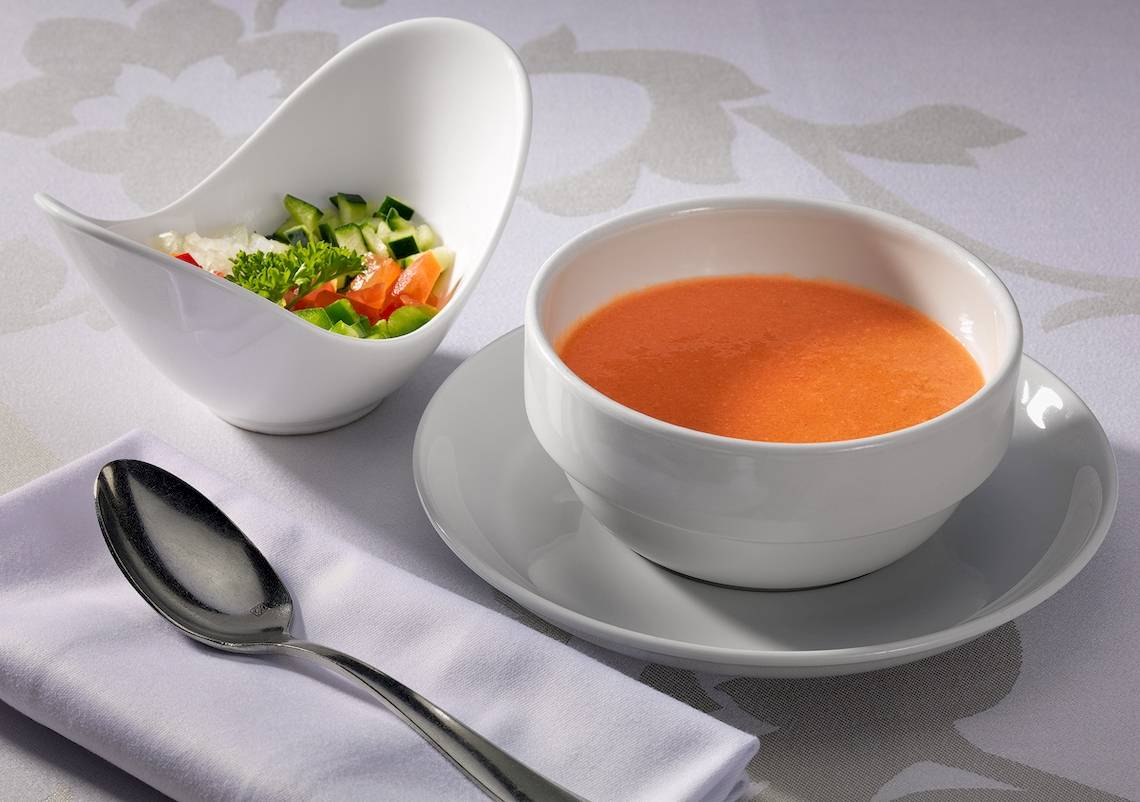 Ein weißer Teller mit einer weißen Schüssel Tomatensuppe und Salat.
