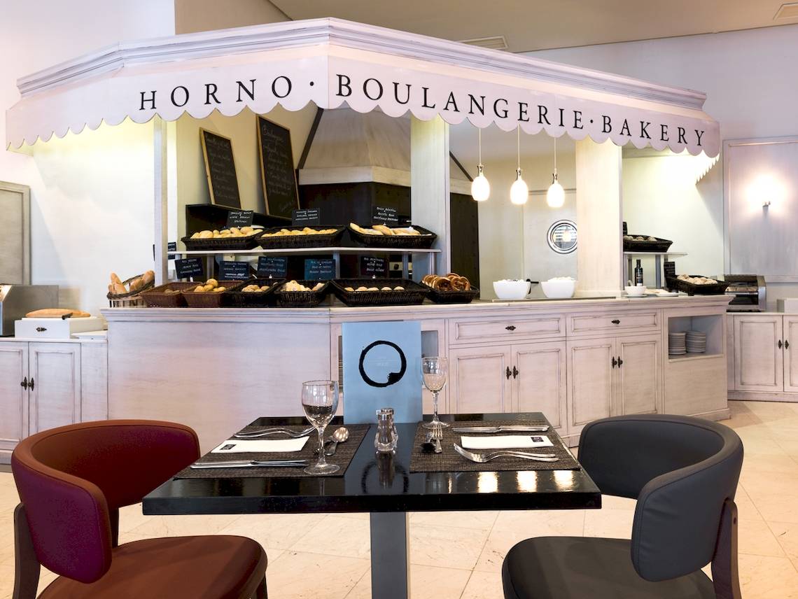Innenansicht der Bäckerei und des Cafés im H10 Estepona Palace mit Tischen und Stühlen.