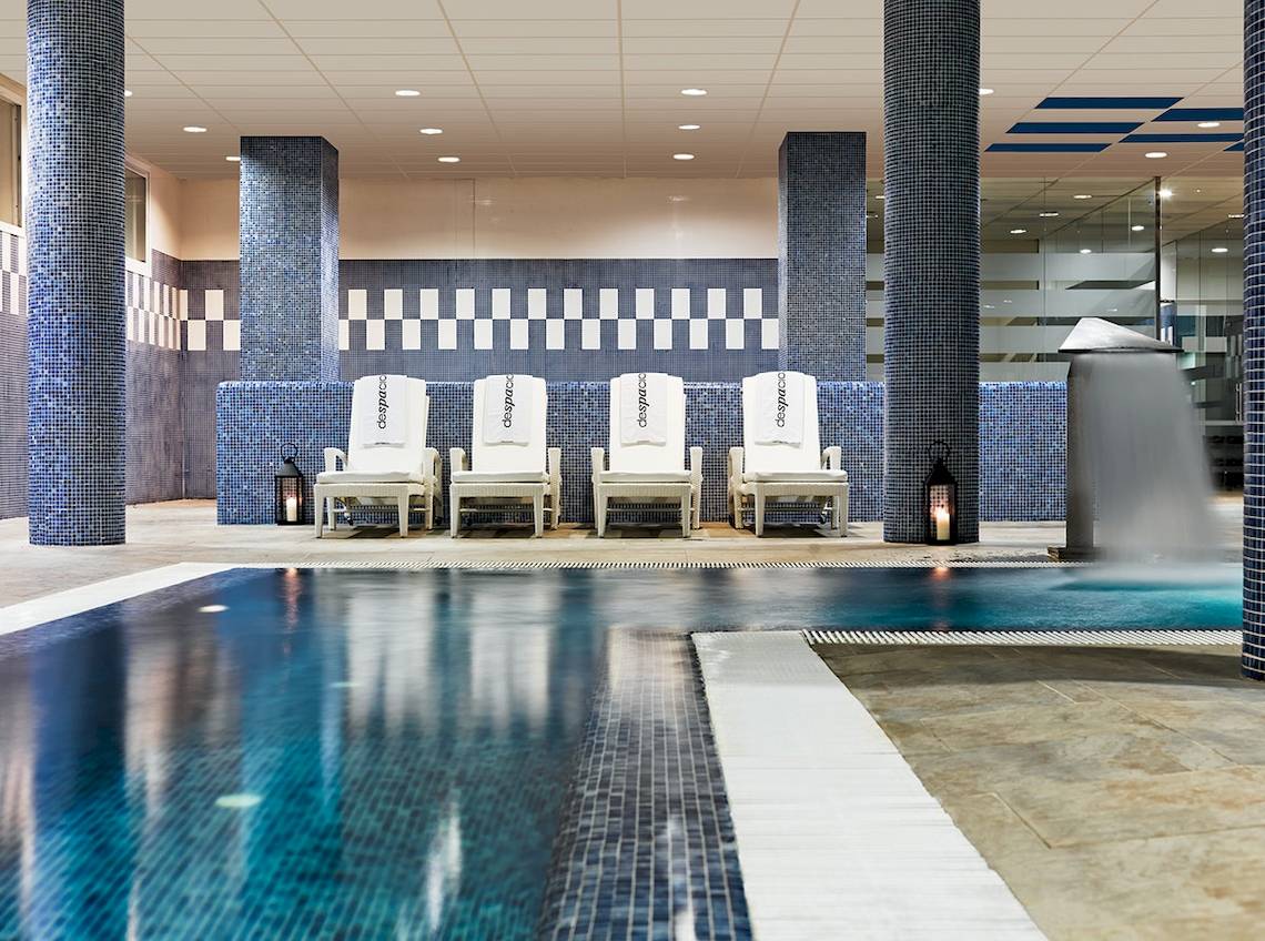 Innenpool des H10 Estepona Palace mit weißen Liegen und blauen Säulen