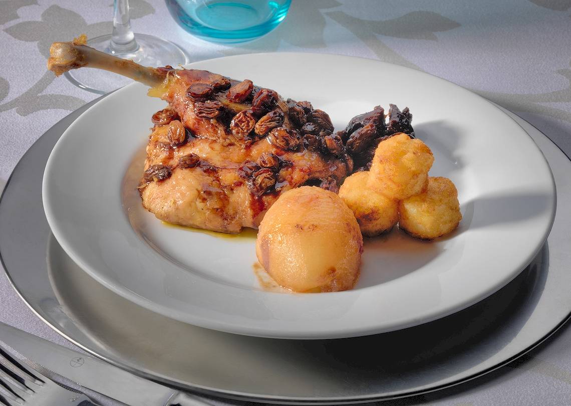 Gebackenes Huhn mit Rosinen und Kartoffeln auf einem weißen Teller.