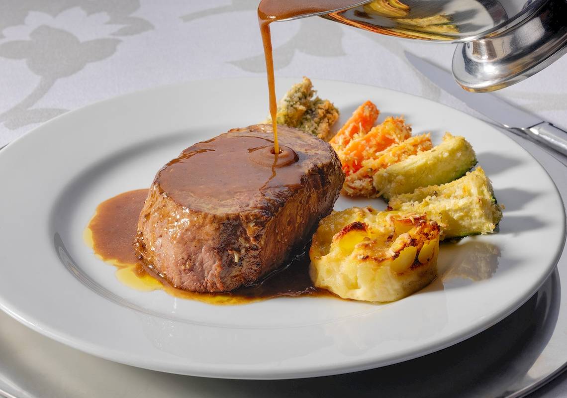 Ein Gericht wird im H10 Estepona Palast serviert, bestehend aus Fleisch, Gemüse und Soße.