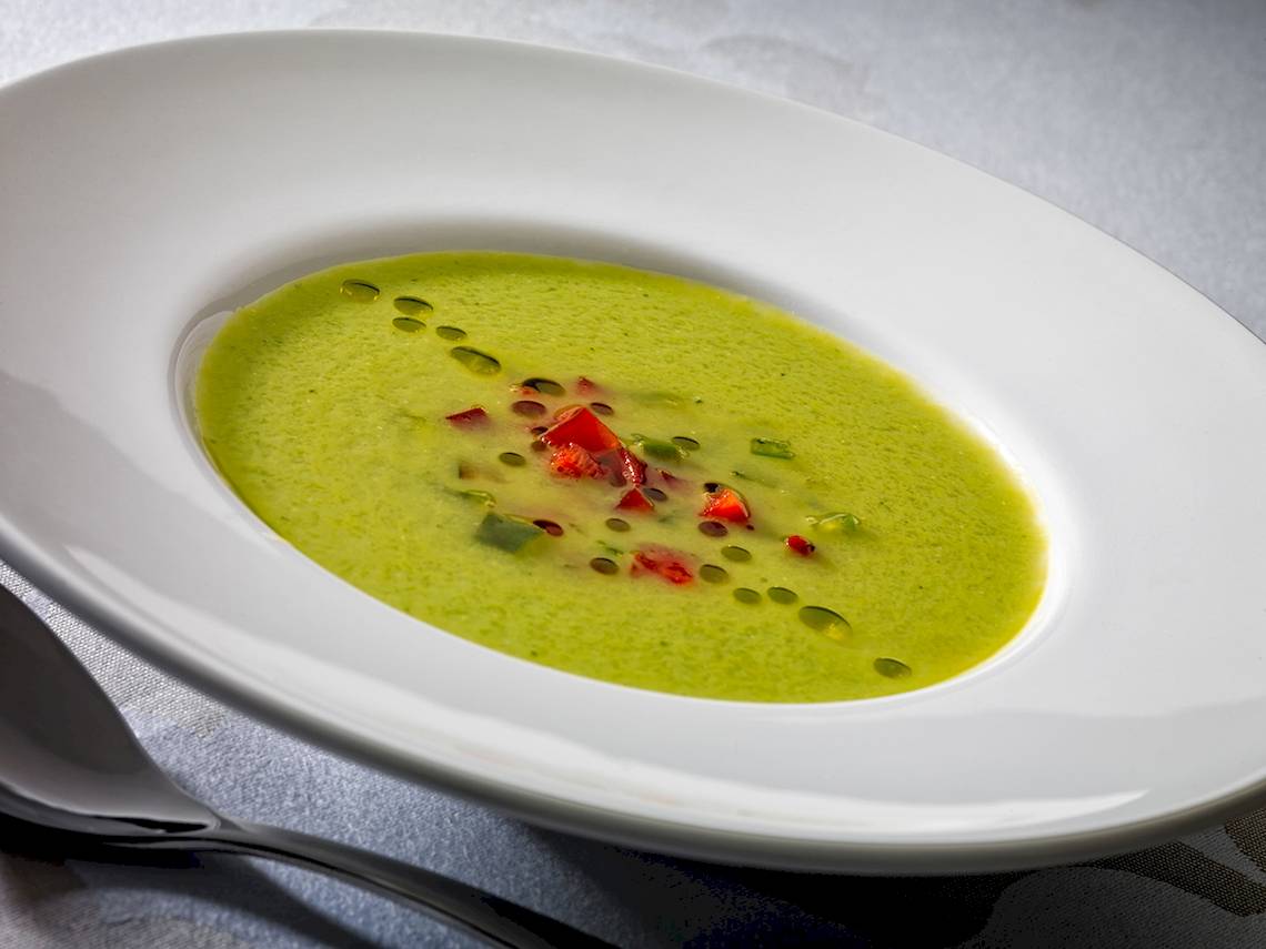 Grüne Suppe in einem weißen Teller mit roten Paprikaschoten und grünem Blatt.