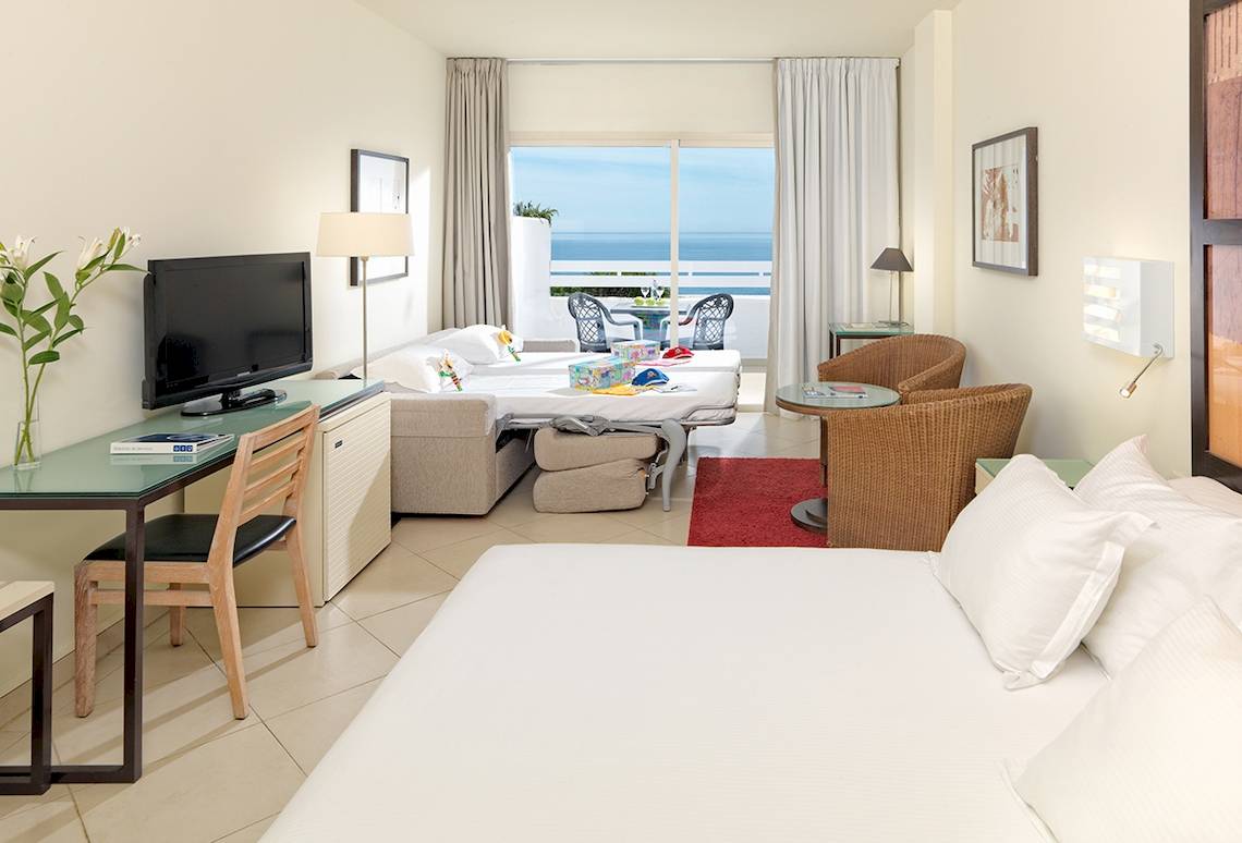 Doppelzimmer im H10 Estepona Palace mit Meerblick, inklusive Wohnzimmer, zwei Betten, Balkon und Fernseher.