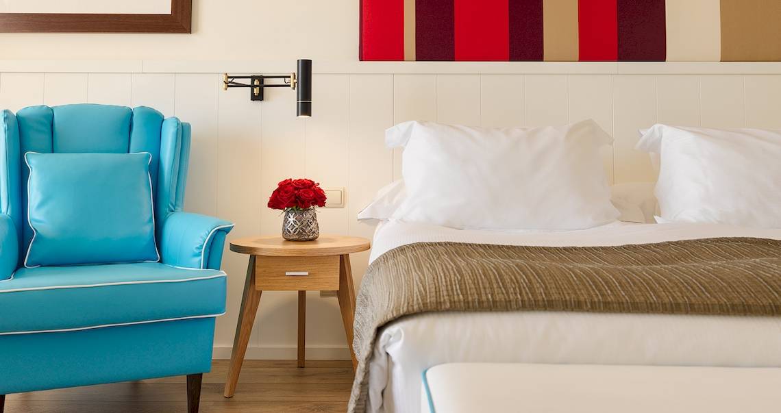 Schlafzimmer im H10 Estepona Palace mit einem Bett, einem blauen Stuhl und einem Nachttisch mit Rosen.