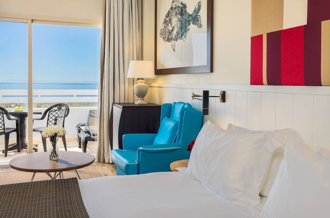 Zimmer im H10 Estepona Palace mit Meerblick, inklusive eines Bettes, eines blauen Sessels, eines Tisches mit Blumenvase und einer Aussicht auf das Meer.