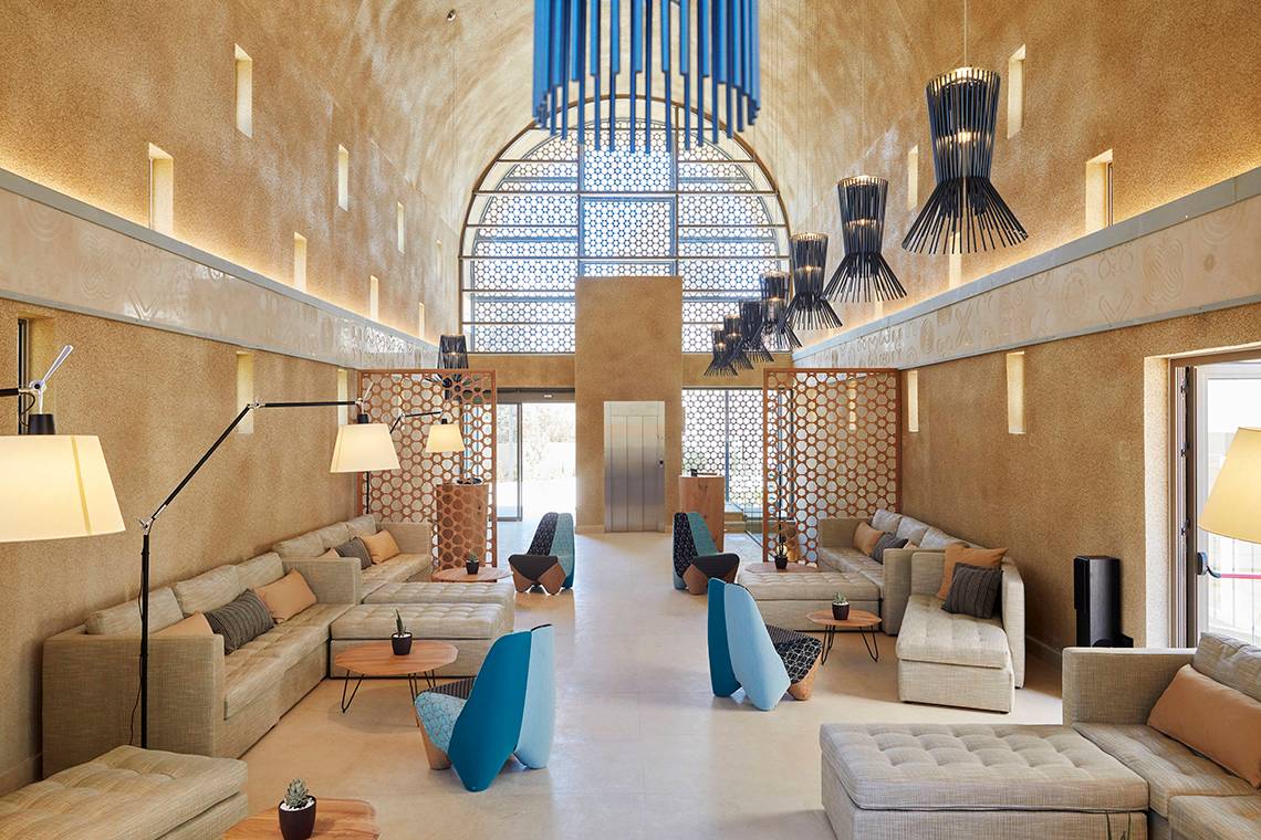 Lobby des Domes Noruz Chania, Autograph Collection mit Sofas, Lampen und einem großen Bogenfenster.