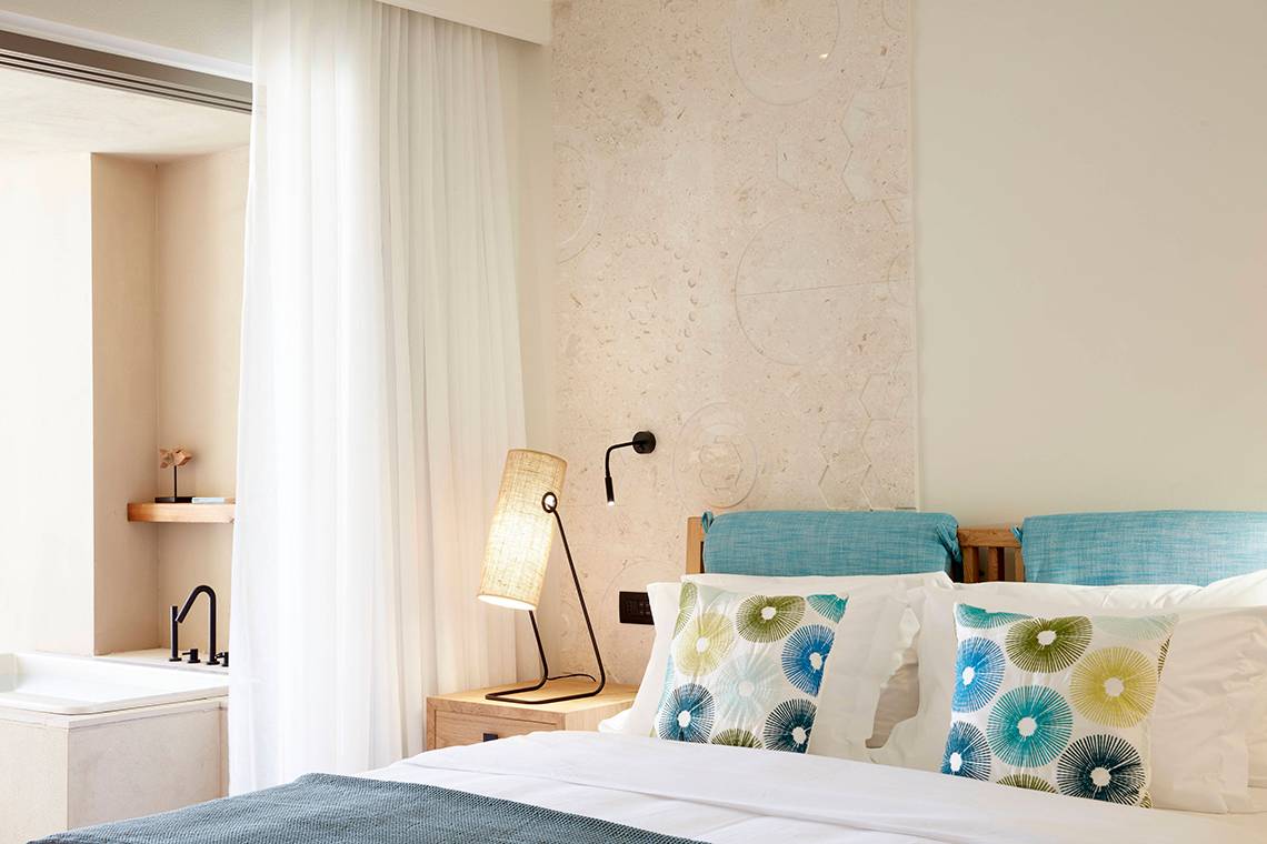 Schlafzimmer im Domes Noruz Chania mit weißen Wänden, blauen Kissen und einem weißen Bett.