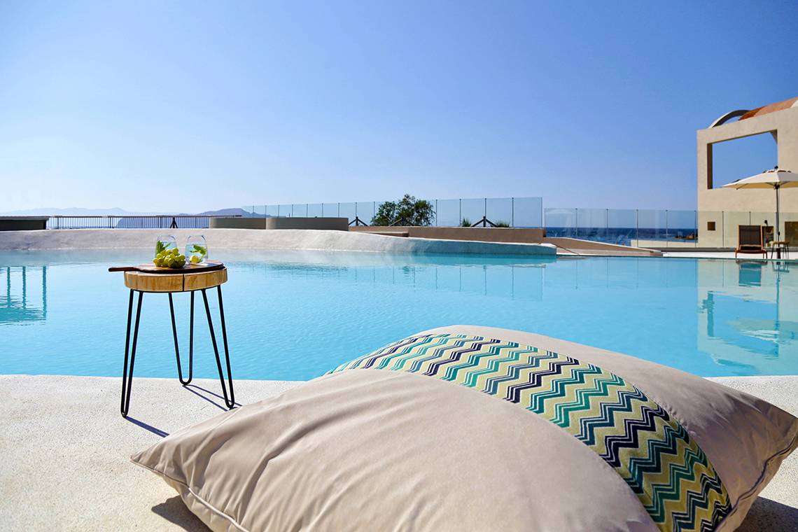 Poolszene im Domes Noruz Chania, Autograph Collection mit Getränken auf einem Tisch und Kissen.