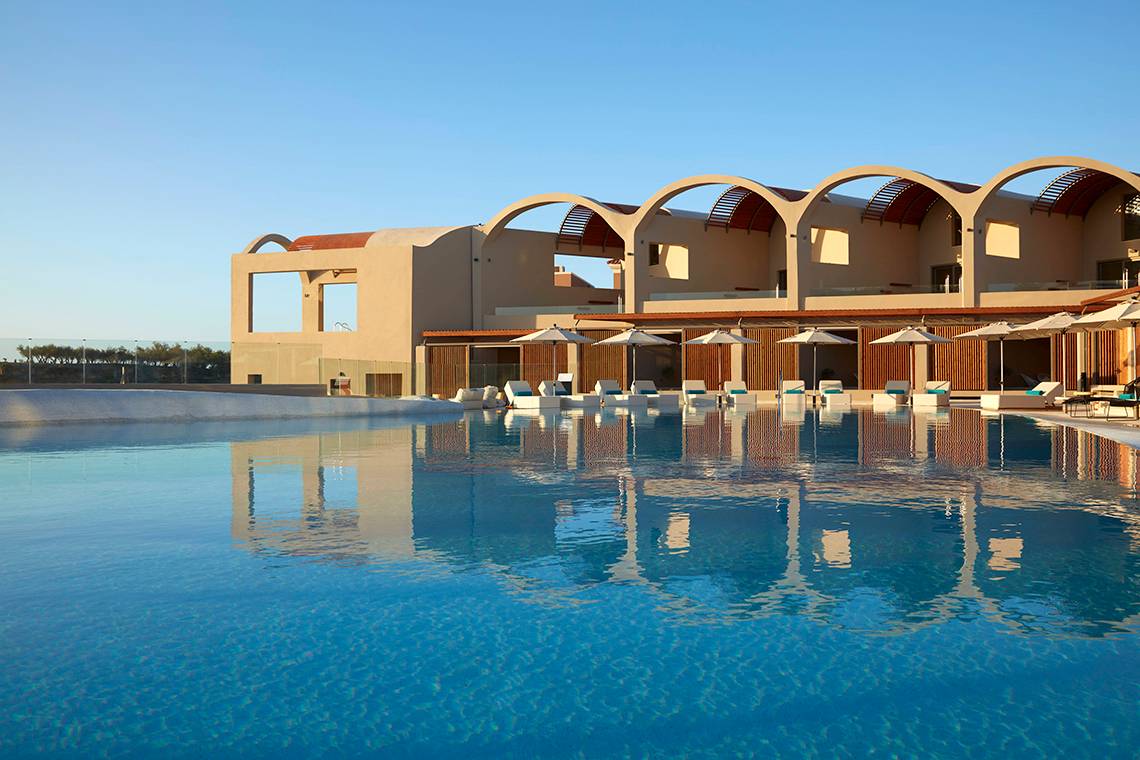 Außenansicht des Domes Noruz Chania Pools mit Sonnenliegen und Schirmen