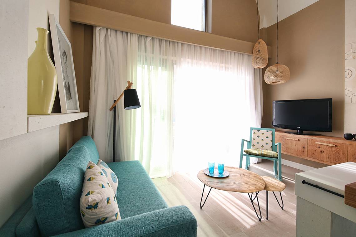 Ein Wohnzimmer im Domes Noruz Chania mit einem blauen Sofa, einem Couchtisch und einer Fernseher.