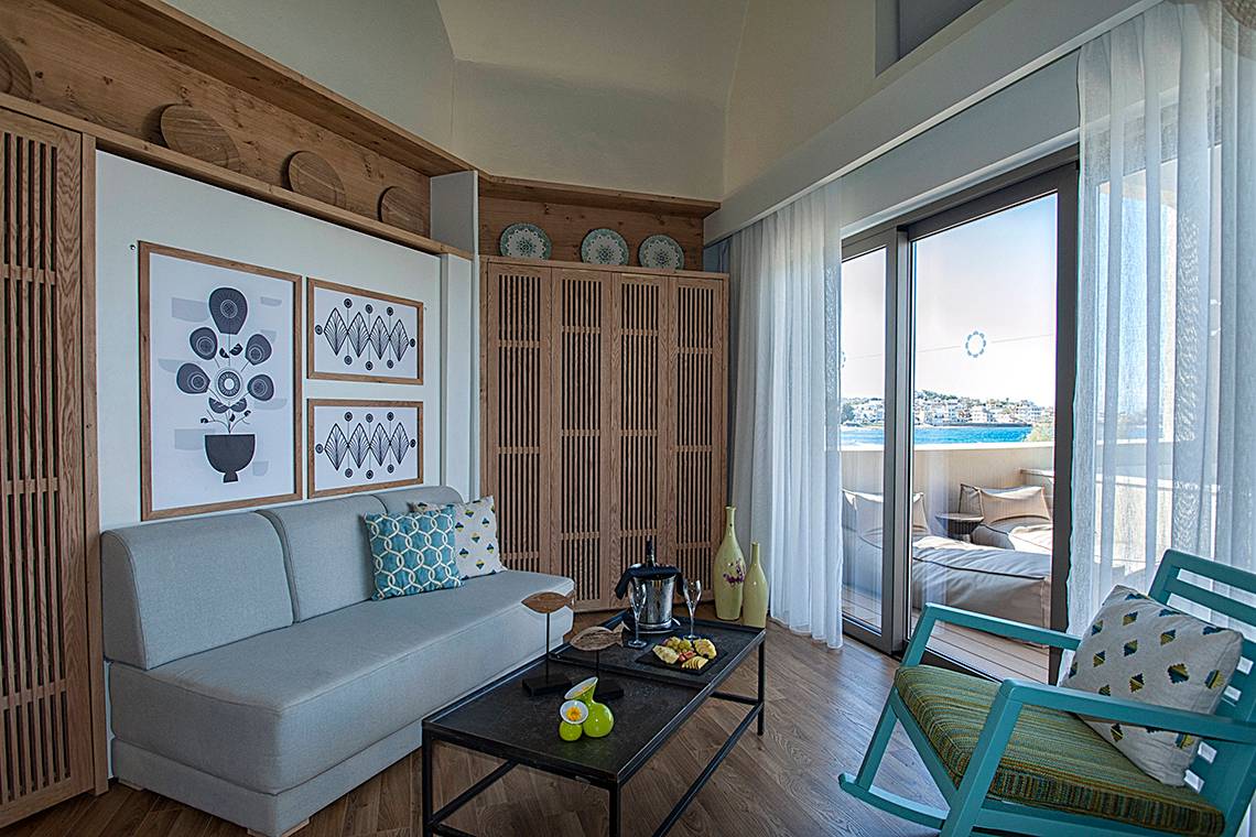 Innenraum der Suite im Domes Noruz Chania mit Sofa, Tisch, Balkon und Meerblick.