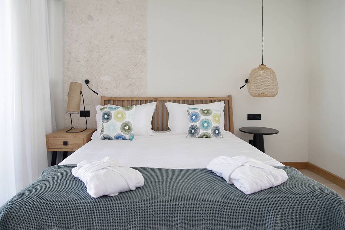 Schlafzimmer im Domes Noruz Chania, Autograph Collection mit weißen Bettwäsche, zwei Nachttischen und dekorativen Lampen.