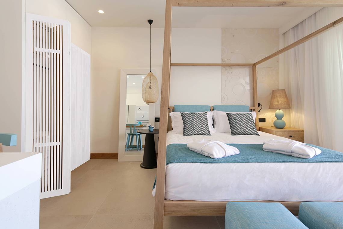 Schlafzimmer im Domes Noruz Chania Hotel mit Himmelbett, blauen Kissen und weißen Decken.