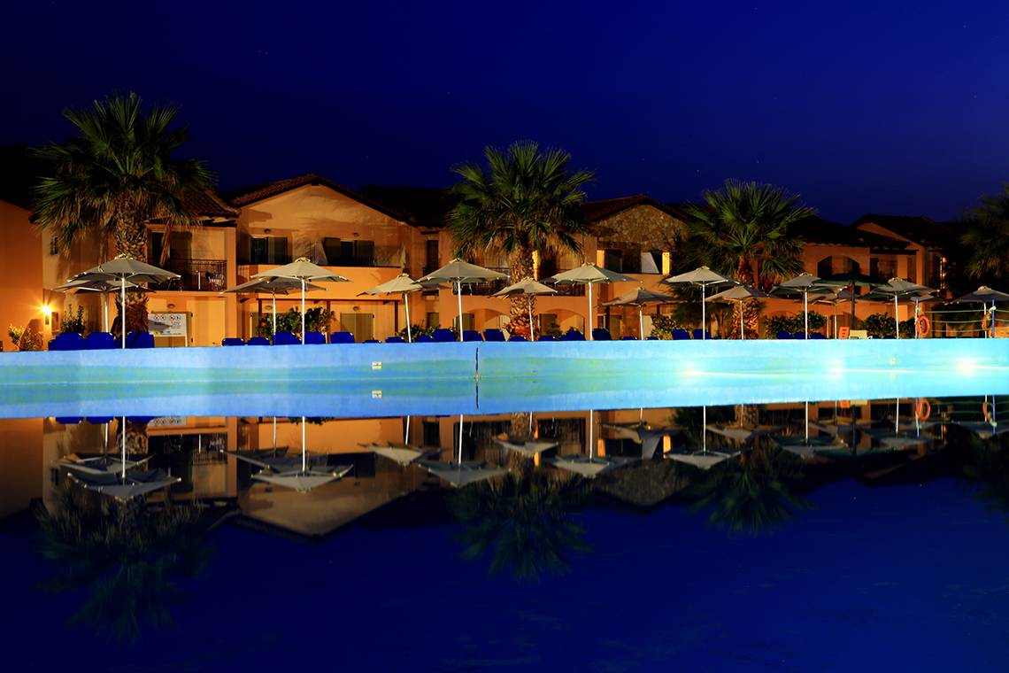 Ein großer Swimmingpool mit reflektierten Sonnenschirmen und Gebäuden im Hintergrund bei Nacht im LABRANDA Marine Aquapark.