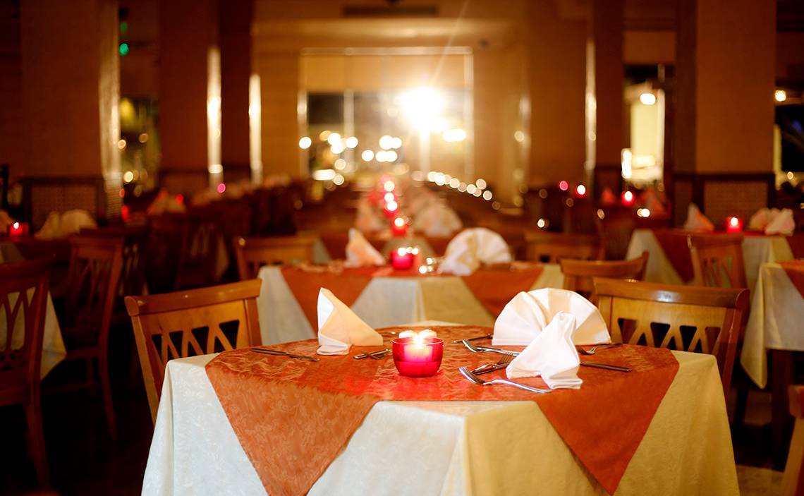 Ein Restaurant im Sharm Club Beach Resort mit gedeckten Tischen, roten Kerzen und dekorativen Lichtern.