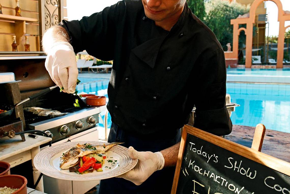 Kochaktion im Orpheas Resort mit Speisen auf einem Teller und einem Mann am Grill.