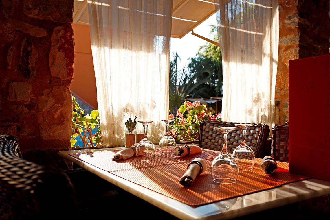 Tisch mit Gläsern und Tischdecke im Orpheas Resort, mit Blick auf eine Terrasse und Pflanzen.