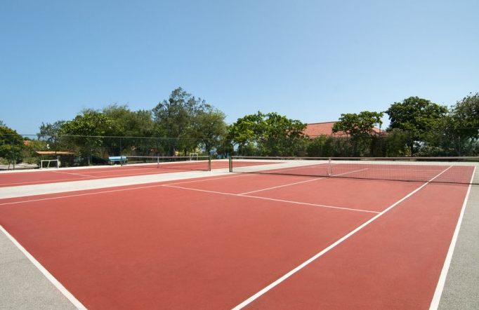 Tennisplatz im Hotel Dreams Curacao Resort, Spa & Casino mit roten Belägen und grünen Bäumen im Hintergrund.