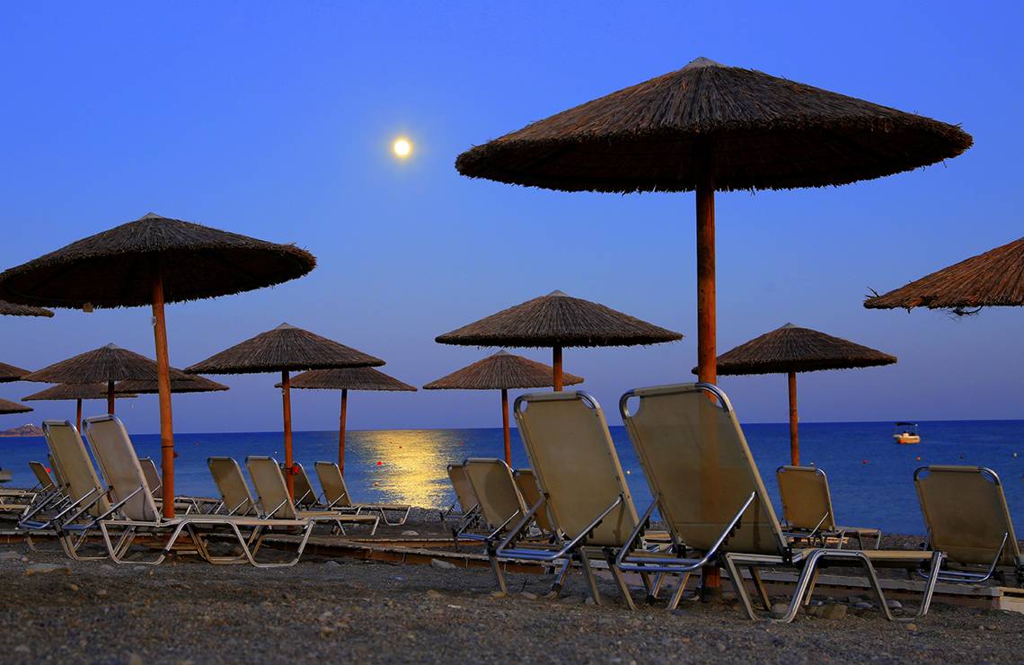 Beim LABRANDA Kiotari Miraluna Resort steht eine Reihe von Sonnenschirmen auf dem Strand bei Mondschein.
