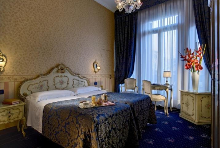 Doppelbett-Zimmer im Hotel Montecarlo mit blauem Teppich und weißen Vorhängen.