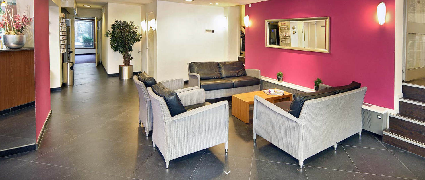 Empfangsbereich des Nova Hotels mit Ledersofas, Tischen und einer rosa Wand.
