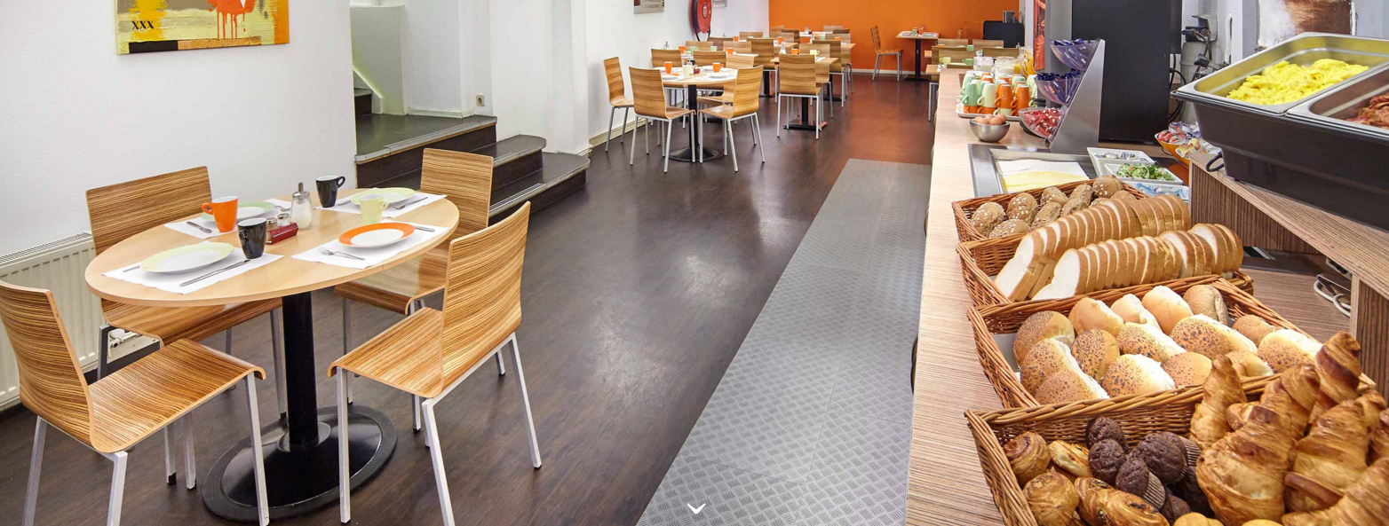 Frühstücksraum im Nova Hotel mit Tischen, Stühlen und Frühstücksbuffet.