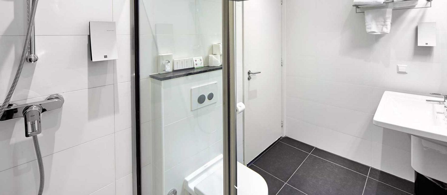 Das Badezimmer im Nova Hotel mit einer Dusche, Toilette, Waschbecken und Fliesenboden.