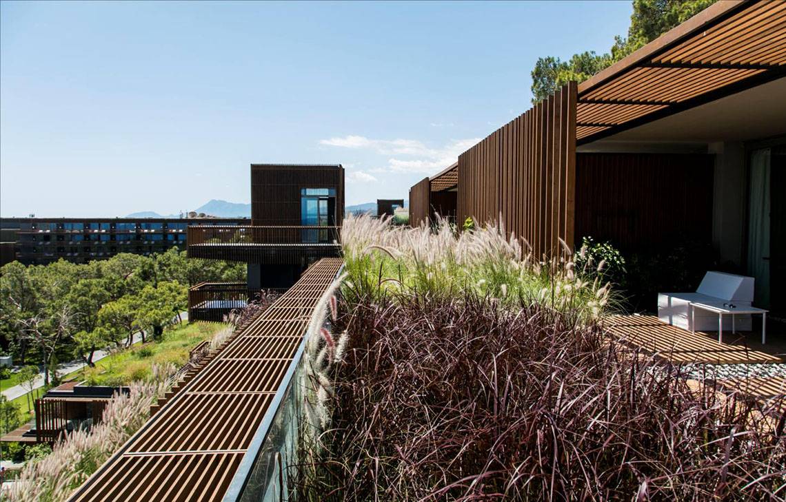 Außenbereich des Maxx Royal Kemer Resorts mit Holzelementen, Pflanzen und Terrassenmöbeln.