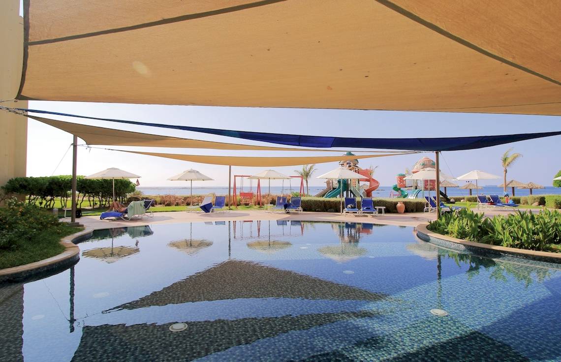 Außenpoolbereich des Wyndham Garden Salalah Mirbat Hotels mit Sonnenschirmen und Liegestühlen.