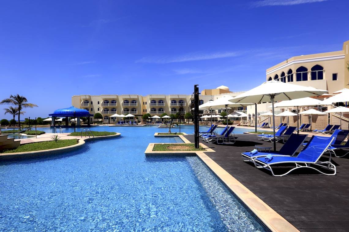 Außenpoolbereich des Wyndham Garden Salalah Mirbat Hotels mit Lounge-Stühlen und Sonnenschirmen.