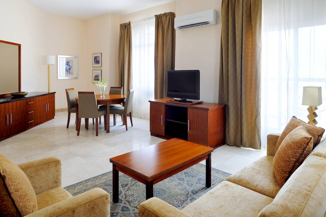 Wohnzimmer des Wyndham Garden Salalah Mirbat Hotels mit Sofa, Tisch und Fernseher.