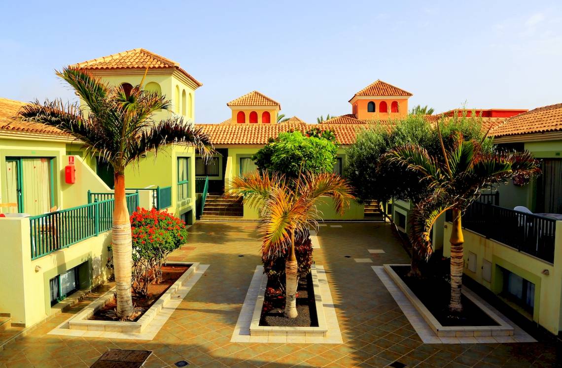 Eingangsbereich des Bluesea Aloe Corralejo Hotels mit Palmen und gelben Gebäuden.