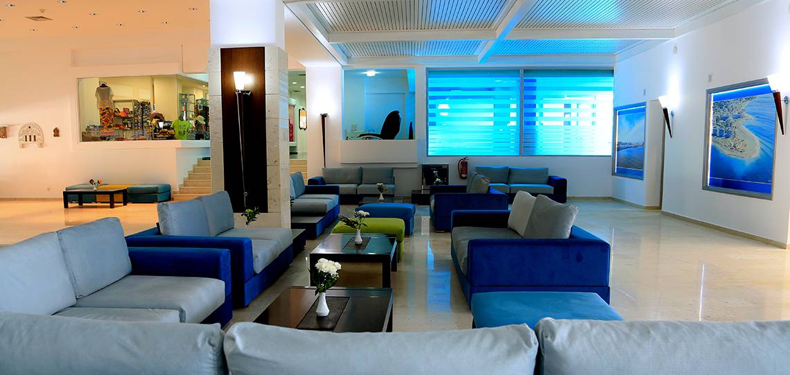 Lobby des Blue Bay Beach Resorts mit blauen Sofas, weißen Wänden und großen Fenstern.