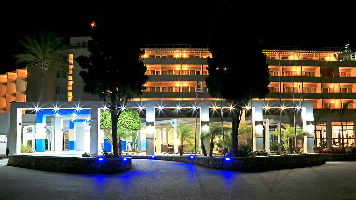 Der Eingang des Blue Bay Beach Resorts in der Nacht mit blauen Lichtern und Bäumen.