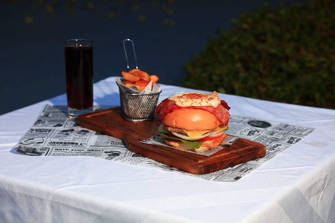 Ein Essen auf einem Holzbrett mit einem Burger, fritiertem Gemüse in einem Korb und einem Glas Getränk.