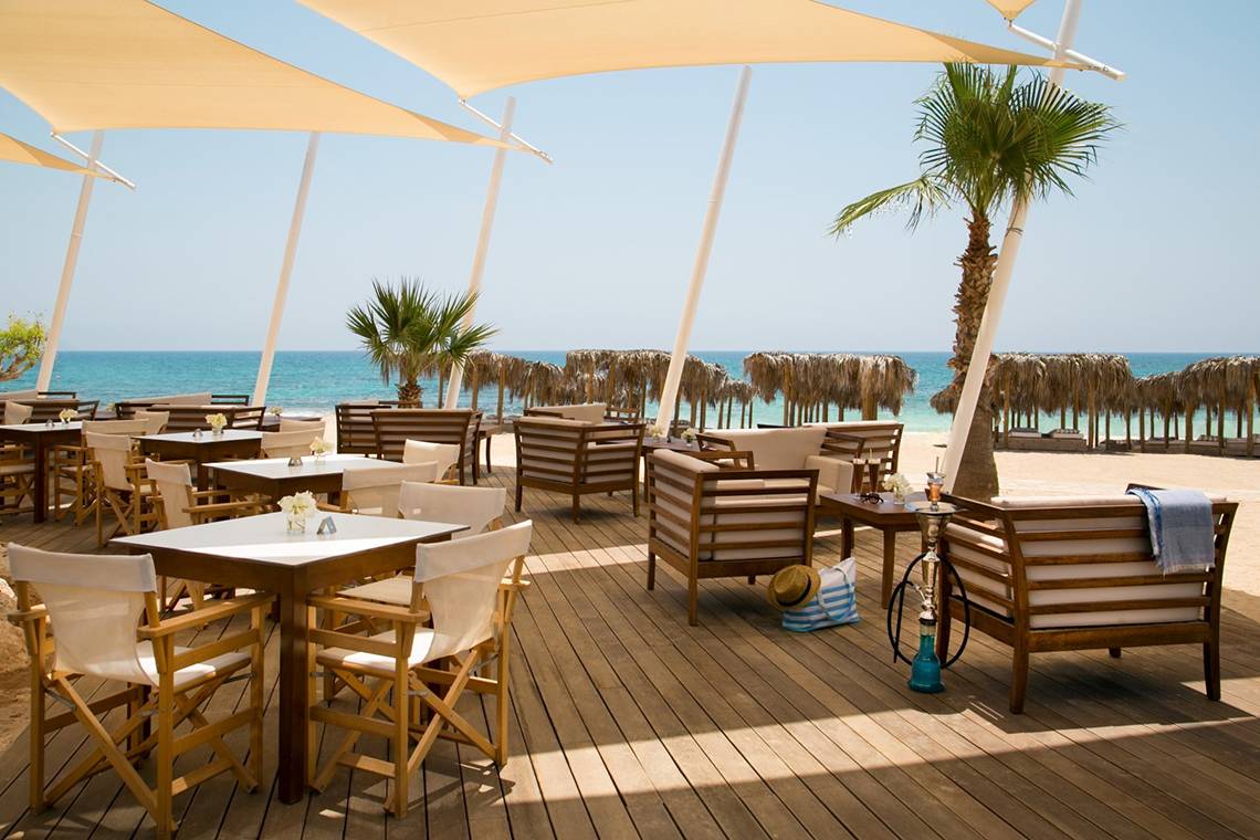 Außenterrasse des Asterias Beach Hotels mit Blick auf das Meer und Palmen.