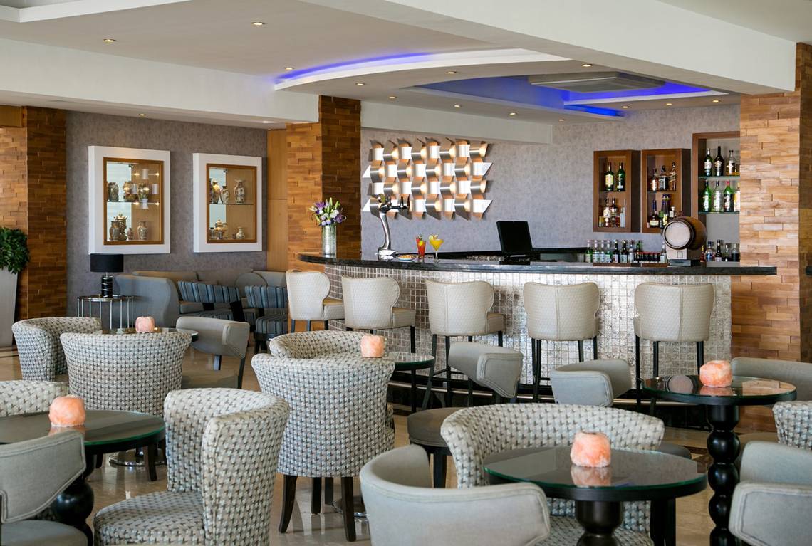 Innenbereich der Bar im Asterias Beach Hotel mit Sitzgelegenheiten und einer Theke.