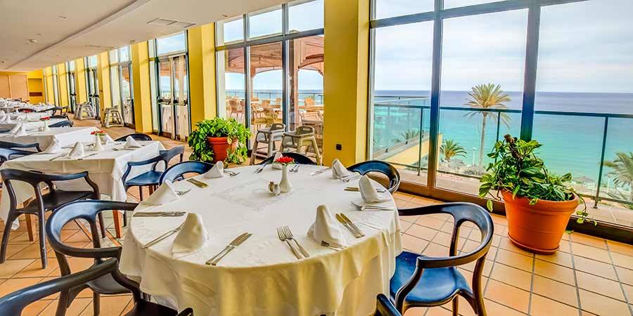 Innenansicht des Restaurants des SBH Club Paraiso Playa mit Blick auf das Meer und Palmen.