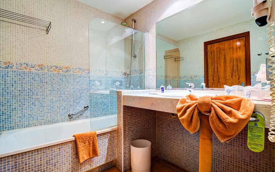 Badezimmer im SBH Club Paraiso Playa Hotel mit blauen Fliesen, Badewanne und Handtüchern.